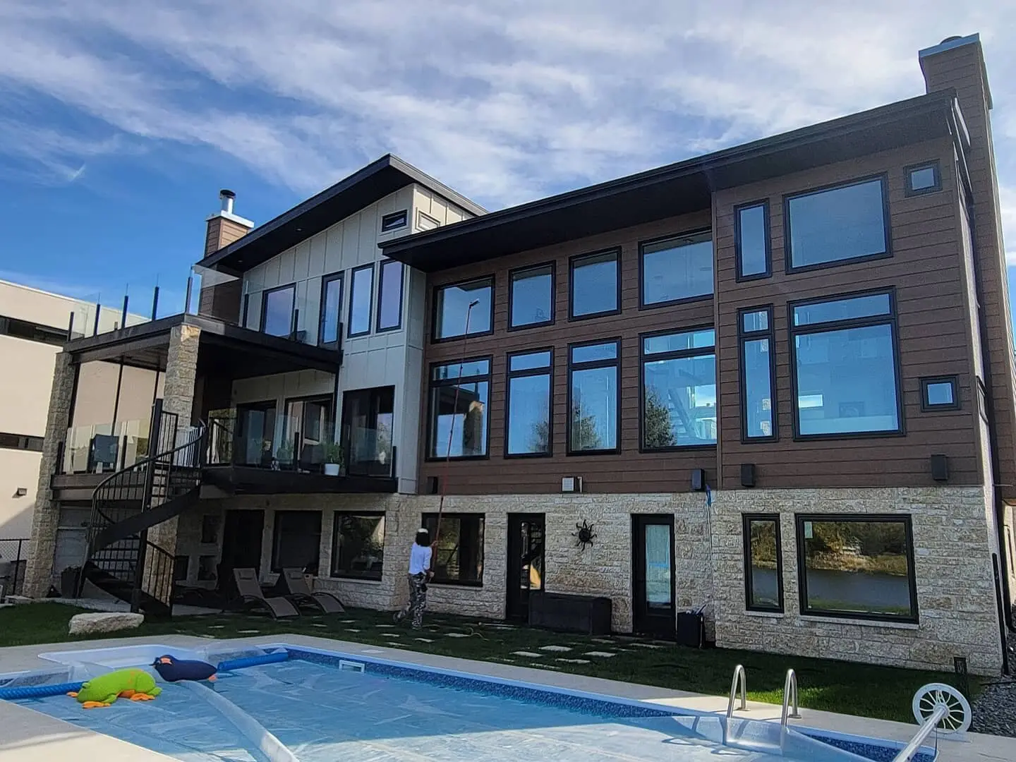 Technician cleaning the windows of a three-storey stone and cedar home from the pool deck